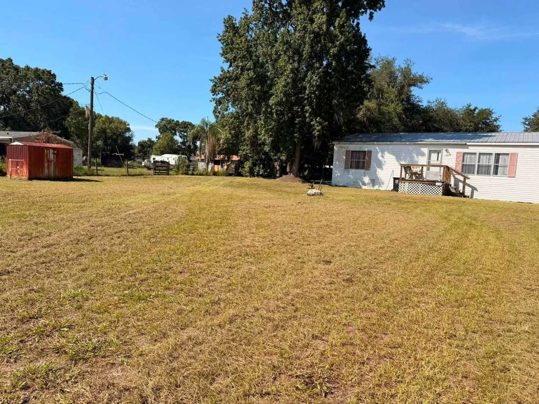 Freshly mowed large lot with a white home and red shed under a clear blue sky